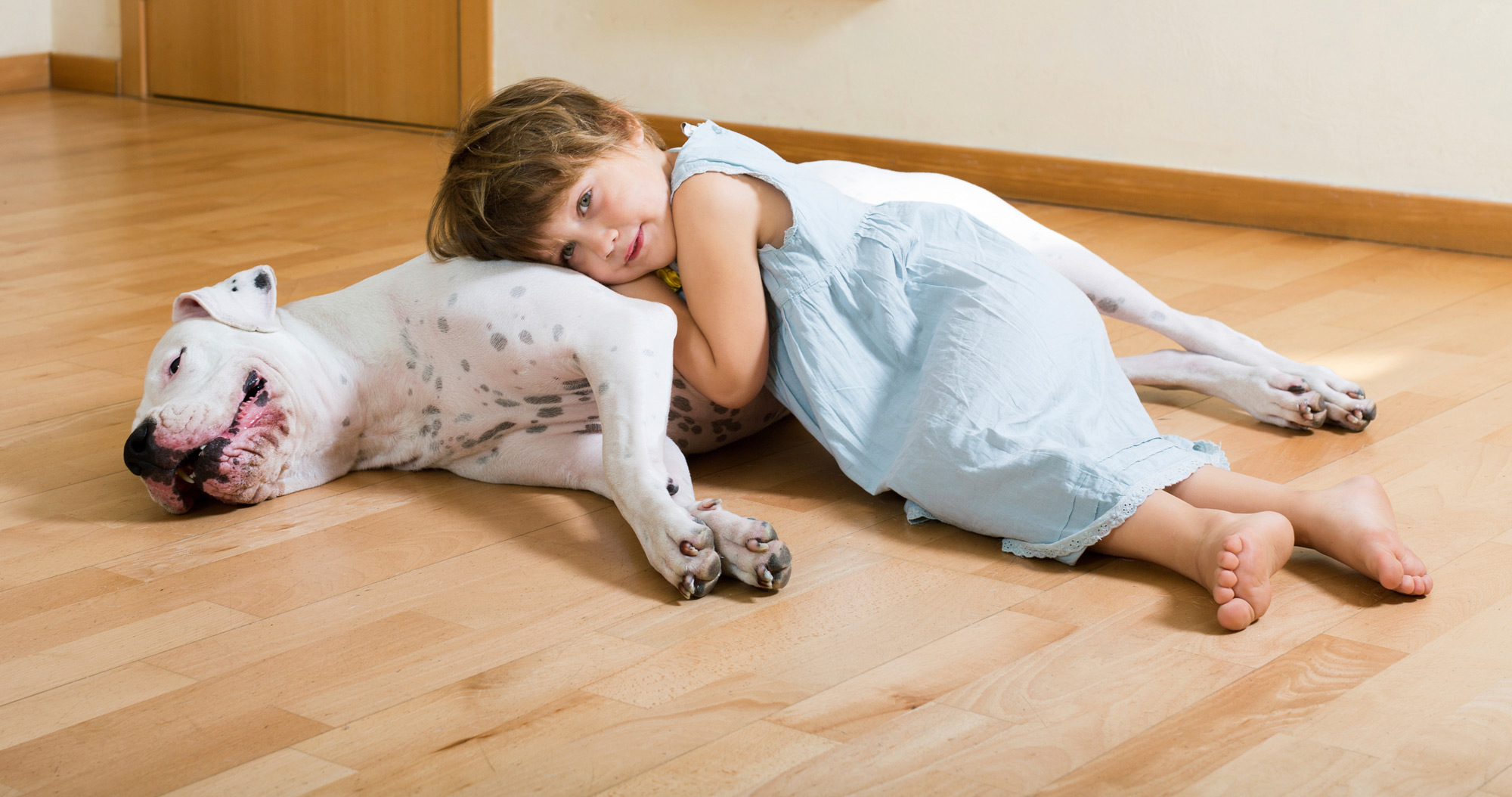 young girl and dog laying on wood floor 
